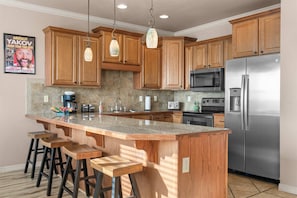 A kitchen with wooden cabinets, a stainless steel refrigerator, a microwave, and a large island with stools. - Yakov's Pointe Pool Access (Hollister)