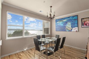 A dining area with a glass table and chairs, large windows with blinds, a chandelier, and a painting on the wall. - Yakov's Pointe Pool Access (Hollister)