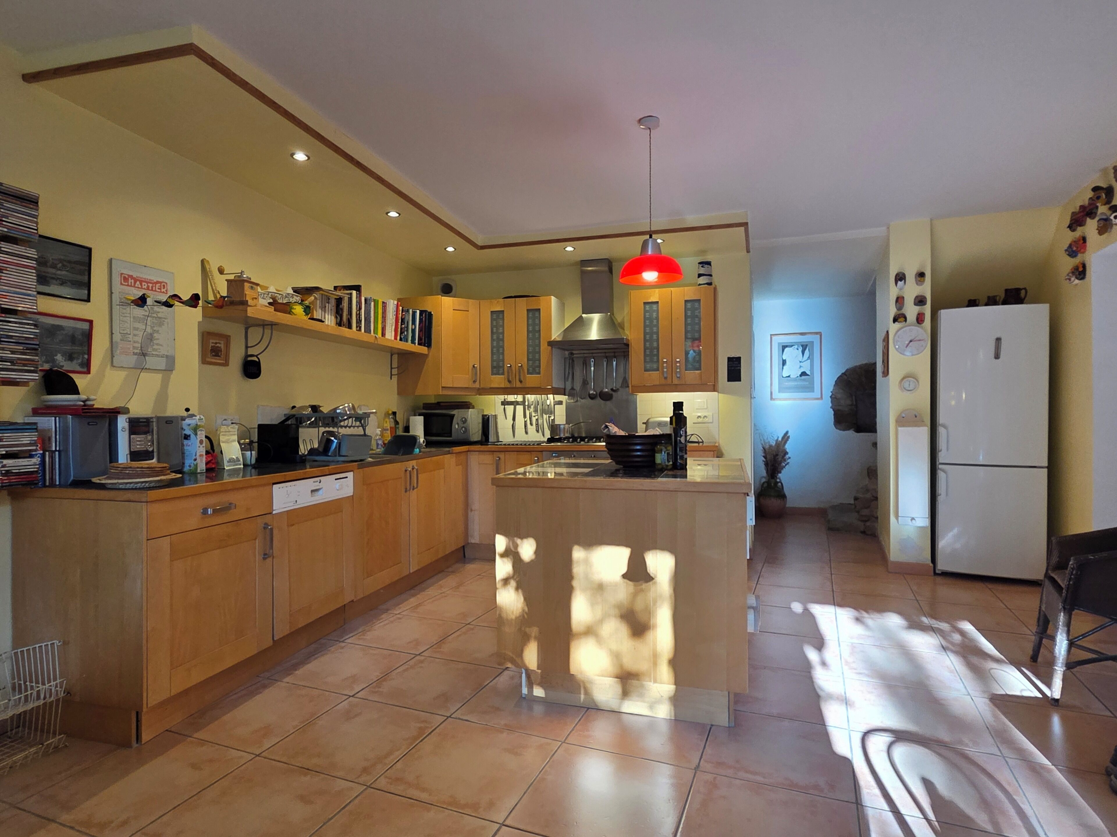 Une cuisine avec des meubles en bois, un îlot central et un luminaire suspendu rouge.