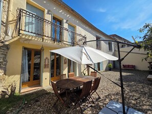 Eine Terrasse mit Tisch und Stühlen, einem weißen Sonnenschirm und ein Balkon mit Geländer.