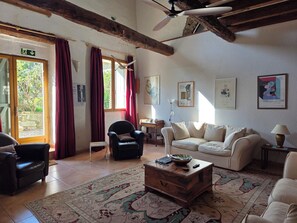 A living room with a wooden coffee table, a sofa, a chair, and a ceiling fan. - Maison Banbury - a large, comfortable and characterful home. (AIGNE)