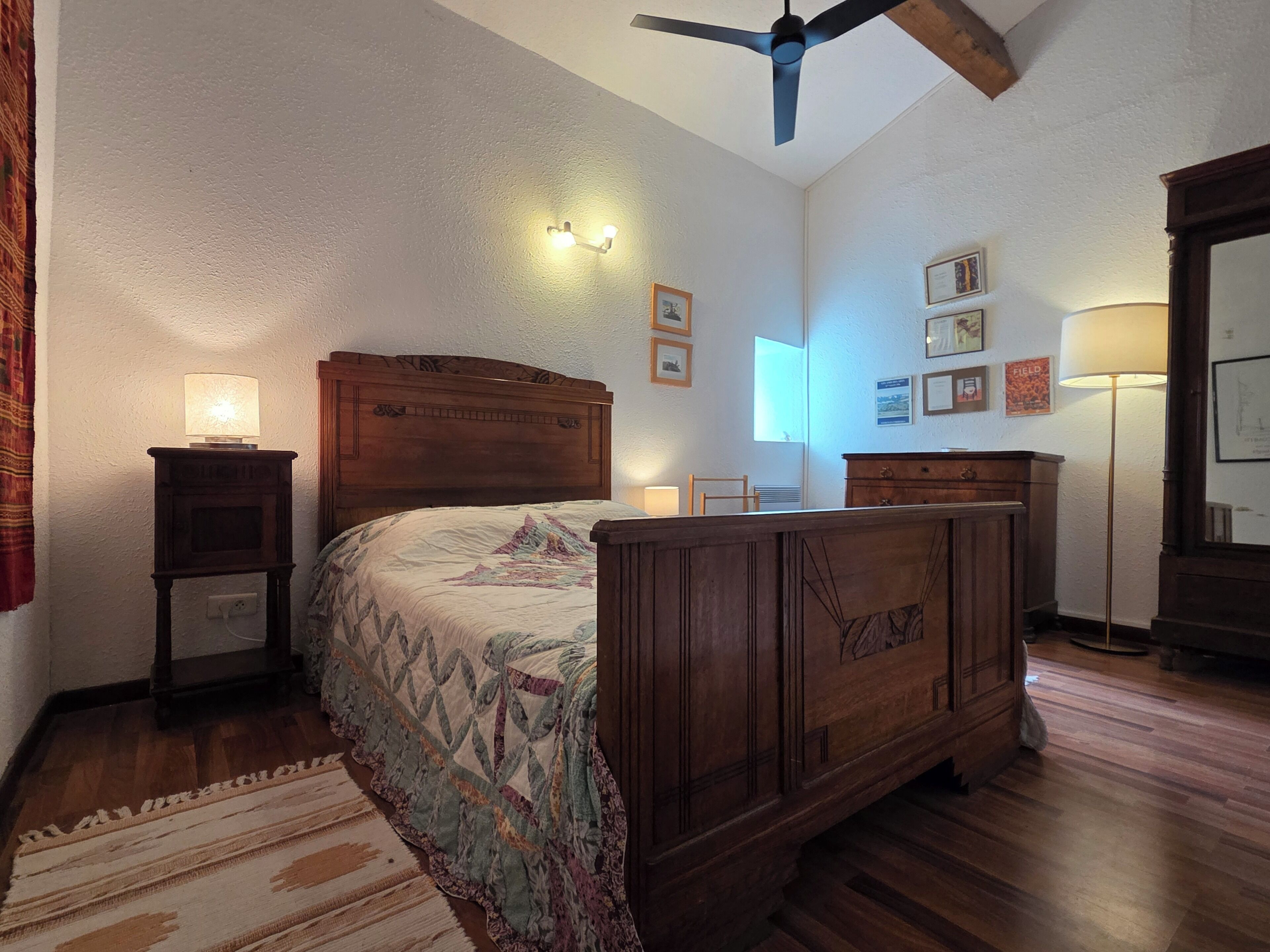 A bedroom with a wooden bed, a nightstand, a ceiling fan, and a window.