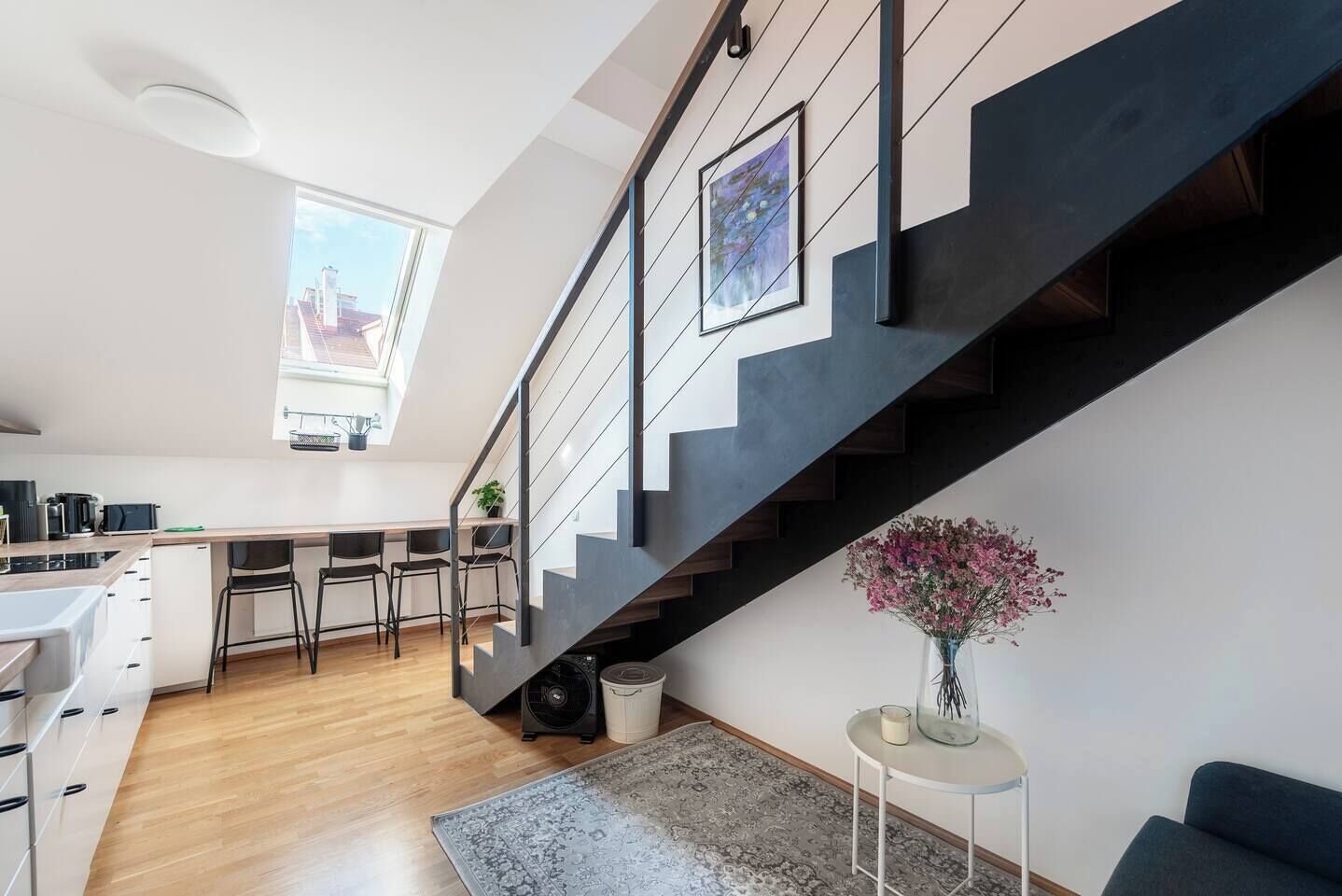 Eine moderne Küche mit Essbereich, einer Treppe und einem Wohnbereich mit Sofa und Blumenvase.