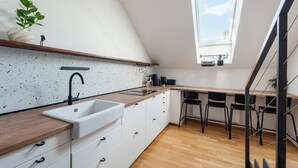 A modern kitchen with a white countertop, a sink, and a window above the dining area. - Bright Duplex Loft near Wenceslas Square (Prague 2)