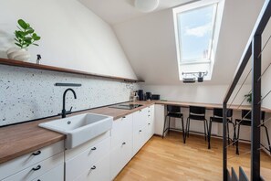 A modern kitchen with a white countertop, a sink, and a window above the dining area. - Bright Duplex Loft near Wenceslas Square (Prague 2)