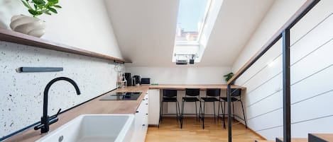 A modern kitchen with a skylight, wooden countertop, and black chairs.