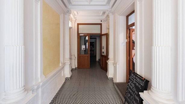 A hallway with white columns, a black and white patterned floor, and a signboard with menu items. - Bright Duplex Loft near Wenceslas Square (Prague 2)
