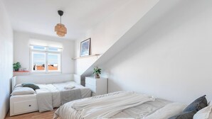 A bedroom with two beds, a window, a bedside table, a nightstand, a hanging light, and a plant. - Bright Duplex Loft near Wenceslas Square (Prague 2)