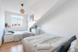 A bedroom with two beds, a window, a bedside table, a nightstand, a hanging light, and a plant. - Bright Duplex Loft near Wenceslas Square (Prague 2)