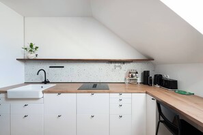 A modern kitchen with a white countertop, a black faucet, and a wooden shelf. - Bright Duplex Loft near Wenceslas Square (Prague 2)