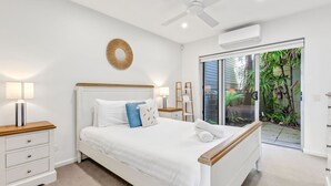 A bedroom with a bed, bedside tables, a ceiling fan, an air conditioning unit, and a view of greenery through a sliding door. - Penthouse 1 | Stylish Beachside Retreat (Sapphire Beach)