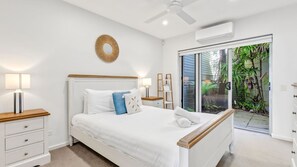 Ein Schlafzimmer mit einem Bett, Nachttischen, einem Deckenventilator, einer Klimaanlage und Blick auf Grün hinter einer Schiebetür.