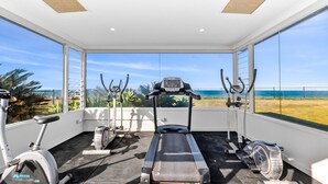A gym with a treadmill, stationary bikes, and elliptical machines, overlooking a beach. - Penthouse 1 | Stylish Beachside Retreat (Sapphire Beach)