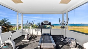 Ein Fitnessraum mit Laufbändern, Ergometer und Crosstrainern, mit Blick auf einen Strand.