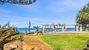 Eine Sitzgelegenheit am Strand mit Blick auf das Meer, ein Weg, der zu der Sitzgelegenheit führt, und Palmen.