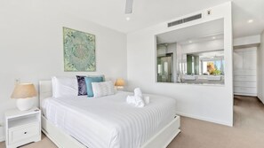 Ein modernes Schlafzimmer mit einem großen Bett, Nachttischlampen, einem Spiegel und Blick ins Badezimmer.