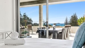 A hotel room with a bed, a table, and chairs, a view of the ocean, and a balcony with plants. - Penthouse 1 | Stylish Beachside Retreat (Sapphire Beach)