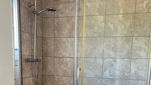 Eine begehbare, gläserne Dusche mit Handbrause und am Wand montiertem Wasserhahn.