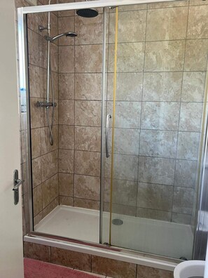 Eine begehbare, gläserne Dusche mit Handbrause und am Wand montiertem Wasserhahn.