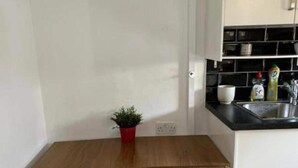 Eine kleine Küche mit Holztisch und -stühlen, einem Blumentopf und einem Spülbecken.