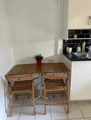 Eine kleine Küche mit Holztisch und -stühlen, einem Blumentopf und einem Spülbecken.