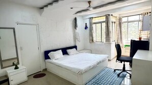 Un dormitorio con cama, escritorio, silla, armario y ventana con cortinas.