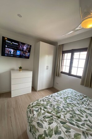 A bedroom with a bed, a dresser, a wardrobe, a television mounted on the wall, and a window with curtains. - für 4 Personen ca. 40 m² in Maspalomas, Gra by Interhome (Maspalomas)