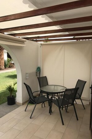 An outdoor patio with a round table and four chairs, a pergola overhead, and a view of a garden. - für 4 Personen ca. 40 m² in Maspalomas, Gra by Interhome (Maspalomas)