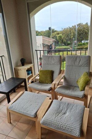 Ein Balkon mit zwei Stühlen, einem kleinen Tisch, einer Topfpflanze und Blick auf eine Wohngegend.