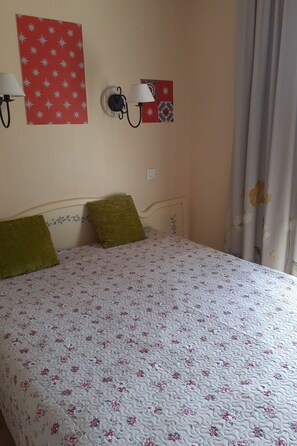 Ein Bett mit floralem Bettbezug, zwei Kissen, eine Wanduhr und eine Wandlampe.