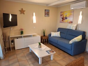 Ein Wohnzimmer mit Flachbildfernseher, einem blauen Sofa, einem Couchtisch und einem kleinen Beistelltisch mit einer Pflanze.