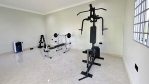 A spacious room with a large window, a bench press, a squat rack, and a small exercise bike. - Ewafe Safari Lodge (Paraa)