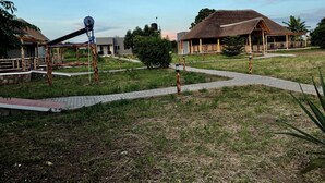 A rural setting with thatched-roof structures, a paved pathway, and a small water pump. - Ewafe Safari Lodge (Paraa)