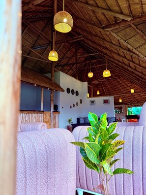 A room with a thatched roof, wicker hanging lamps, and patterned furniture. - Ewafe Safari Lodge (Paraa)