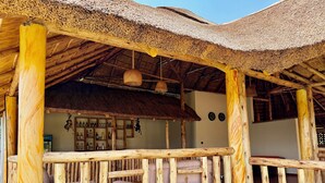 A rustic wooden structure with a thatched roof, a bar area with shelves of bottles, and cushioned seating. - Ewafe Safari Lodge (Paraa)