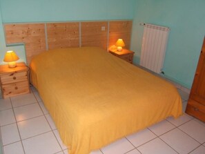 Ein Schlafzimmer mit einem hölzernen Kopfteil, einem Einzelbett mit gelber Bettdecke, zwei Nachttischen mit Lampen und einem Heizkörper an der Wand.
