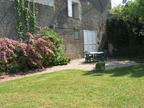 Ein Steinhaus mit einem kleinen Garten, einem Tisch mit Stühlen und einem Fenster mit Fensterläden.