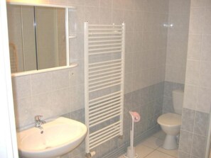 Ein Badezimmer mit einem weißen Waschbecken, einem Spiegel, einem Handtuchhalter und einer Toilette.