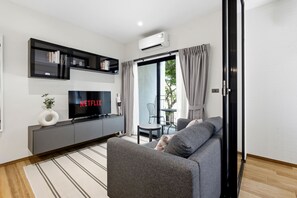 A modern living room with a grey sofa, a flat-screen TV, and a bookshelf. - The Title Halo 1BR Apartment • Pools • 5 Min to Nai Yang Beach (Sakhu)