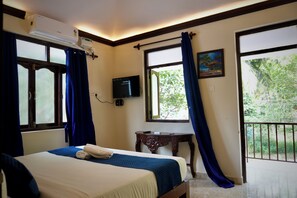 A hotel room with a bed, a television, a small table, and a balcony with curtains.