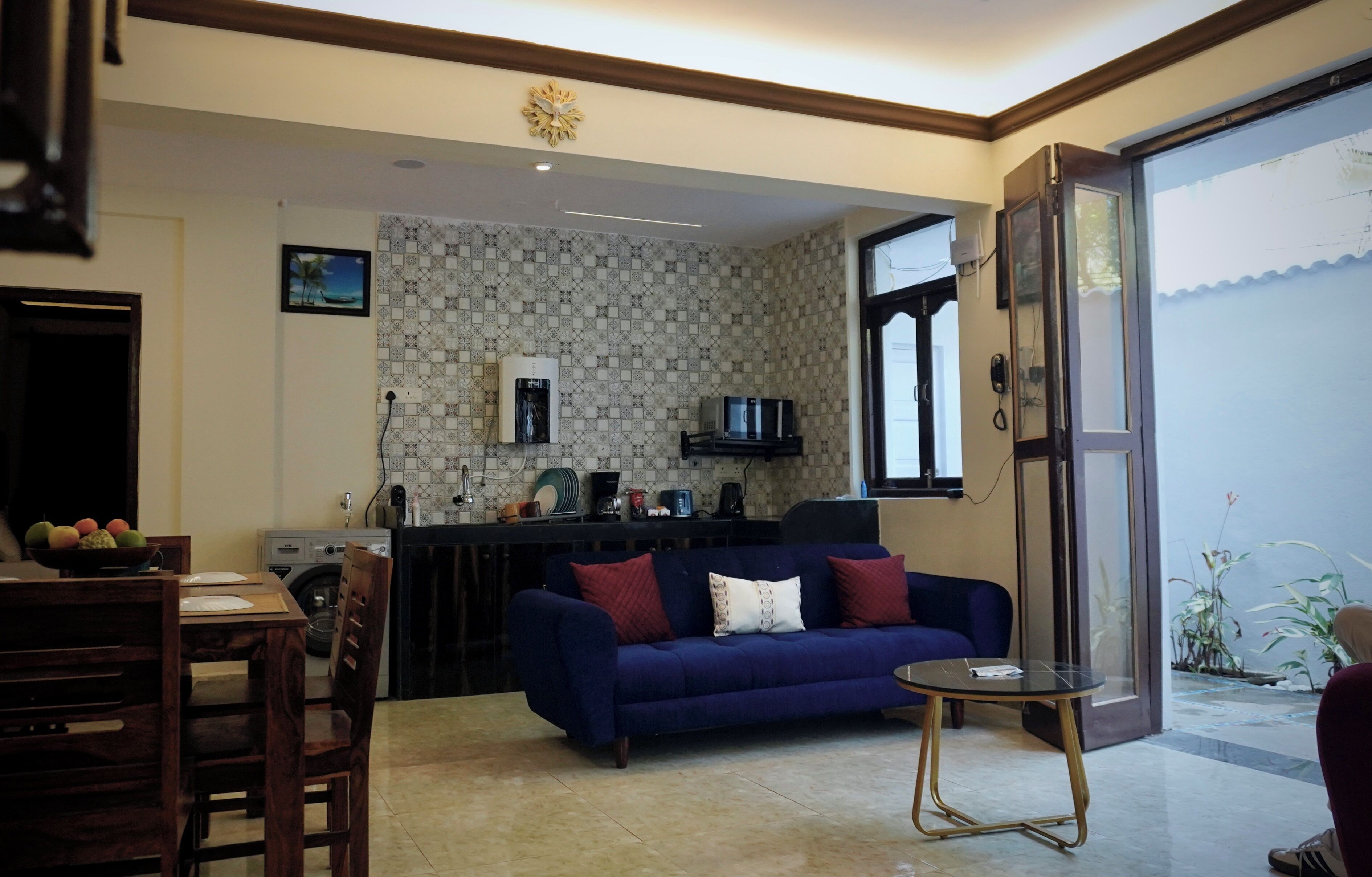 A living room with a blue sofa, a small round table, and a kitchen area with a microwave and water dispenser.