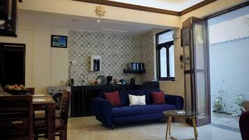 A living room with a blue sofa, a small round table, and a kitchen area with a microwave and water dispenser.