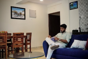 A man sitting on a blue sofa reading a book in a living room with a dining area and a door.