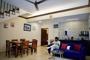 A living room with a dining area, a ceiling fan, a blue sofa, and a kitchen area with a microwave.
