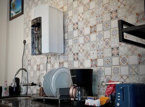 A kitchen with a coffee maker, a dish rack, and a tiled backsplash.