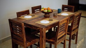 A wooden dining table with four chairs, a fruit bowl, and a blue mug on placemats.