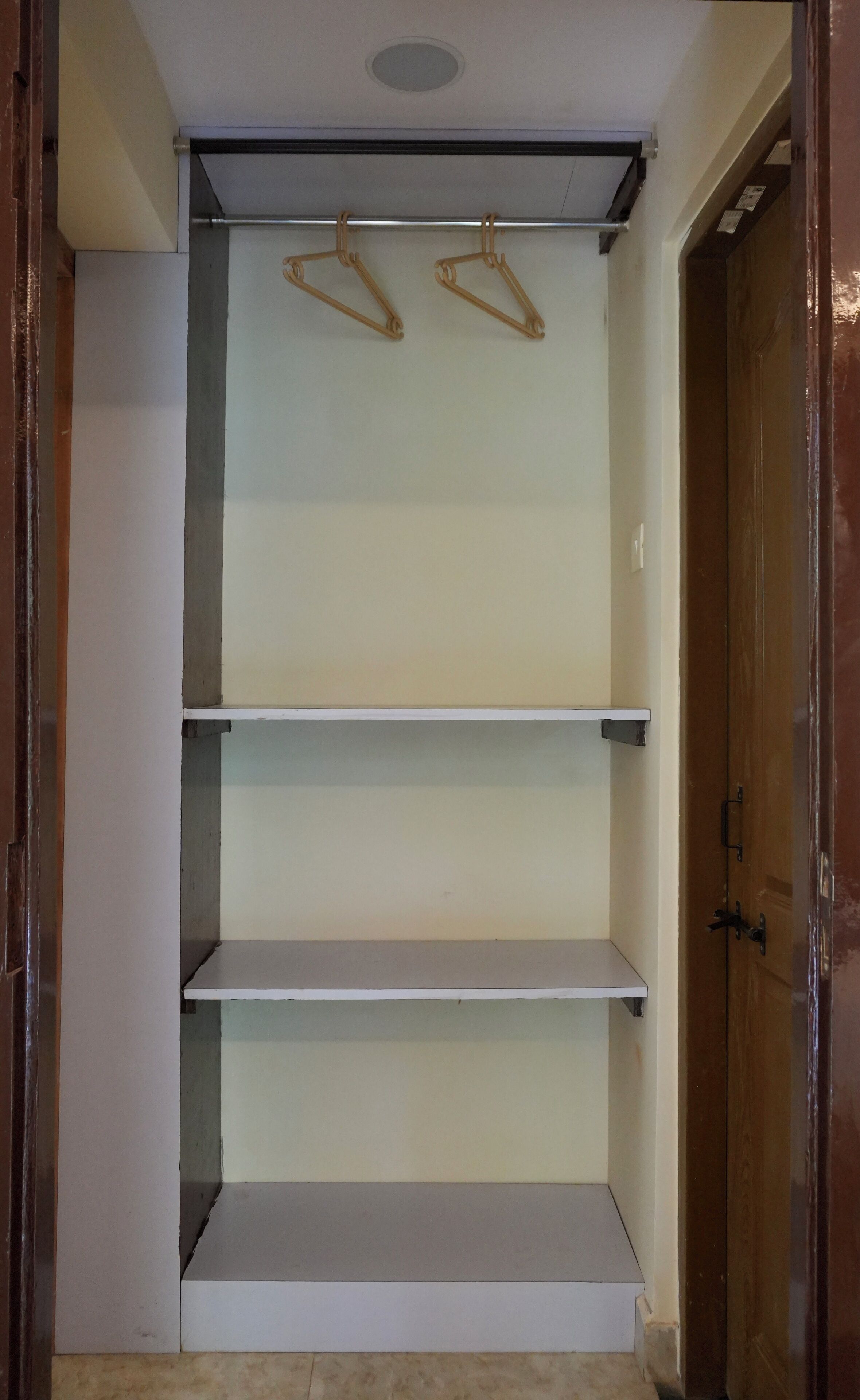 Een kast met drie planken en twee houten kledinghangers.