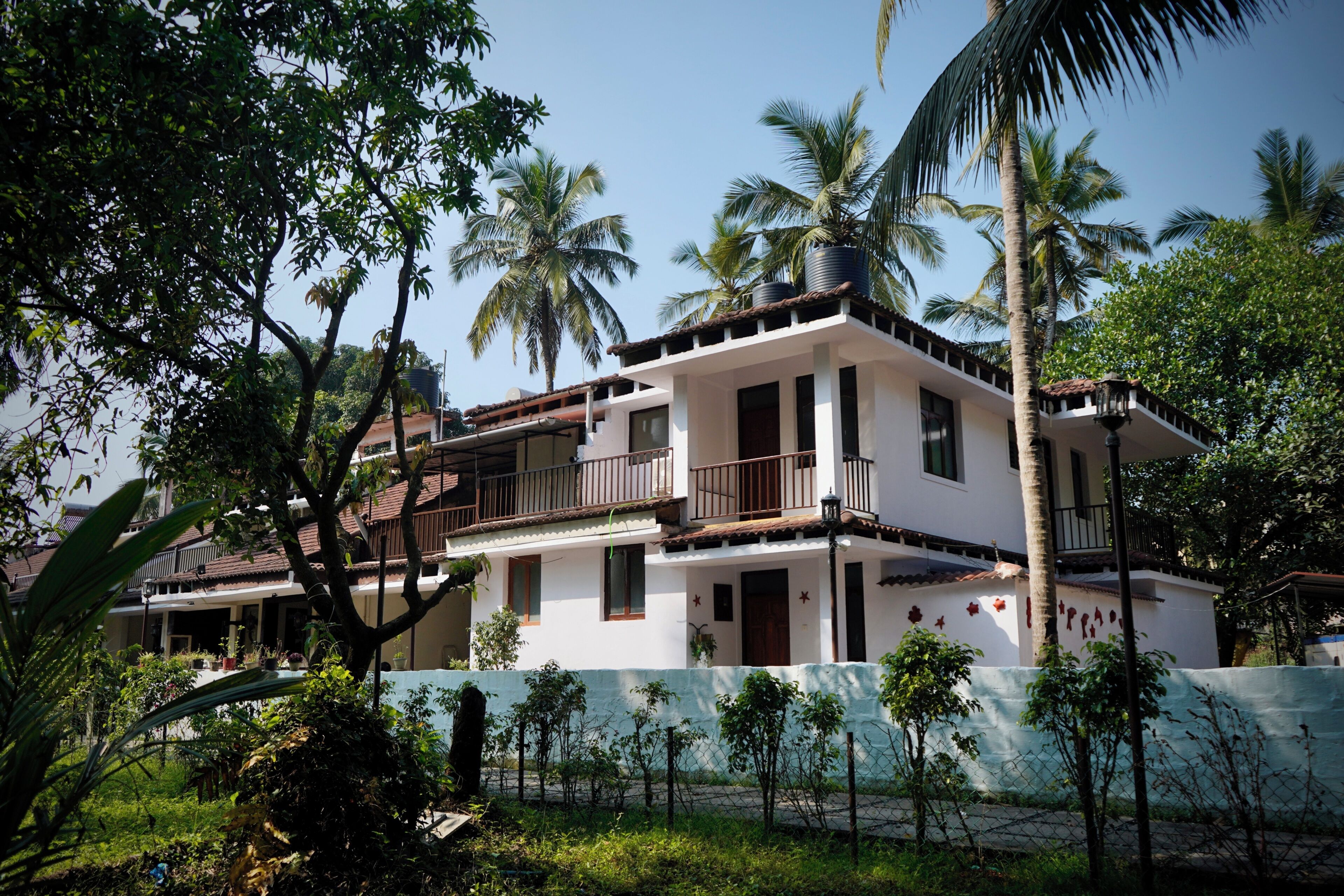 A two-story building with a balcony, surrounded by lush greenery and palm trees.