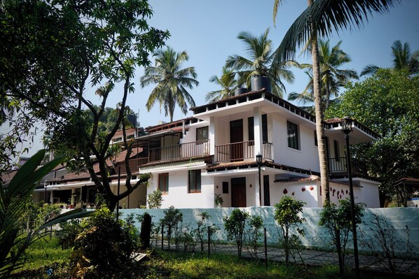 A two-story building with a balcony, surrounded by lush greenery and palm trees.