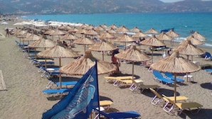 Una platja amb files de sombrerets i gandules, un cel clar i un paisatge de muntanyes al fons.